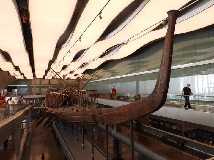 Ancient solar boat displayed inside modern gallery with undulating ceiling panels