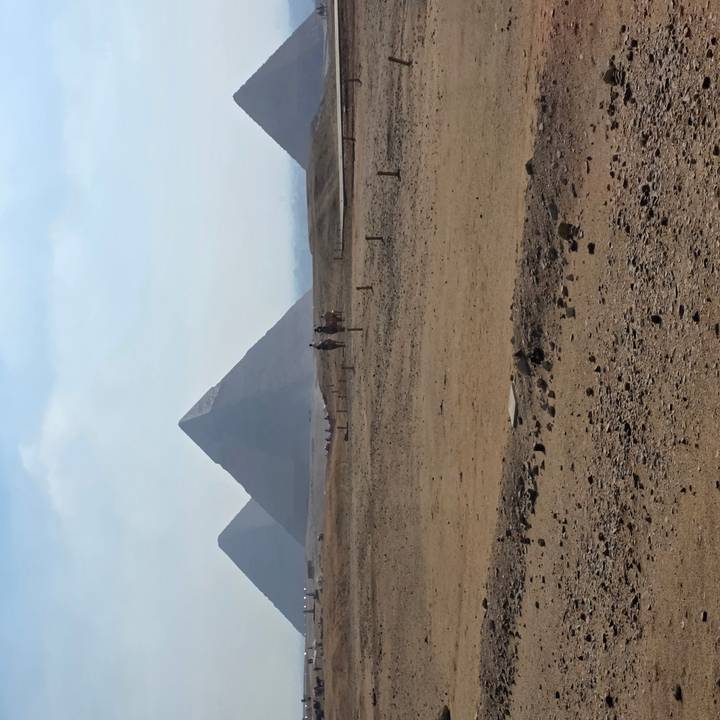 Distant pyramids rising above sandy plateau with hazy morning sky