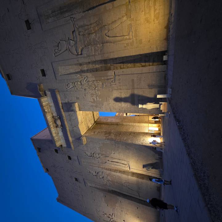 Illuminated entrance of Egyptian temple at blue hour with tall shadow on wall
