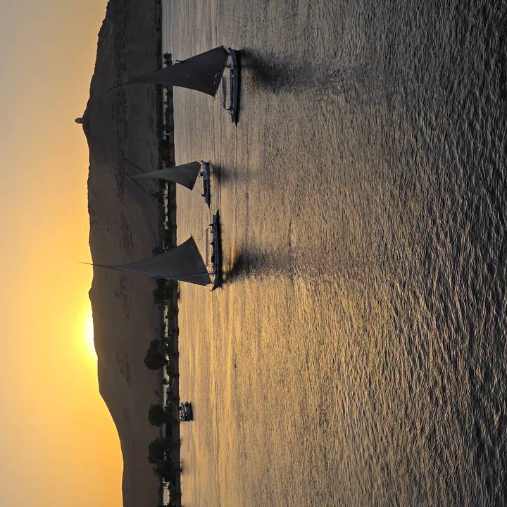 Two feluccas sailing on the Nile at sunset with golden reflections on the water