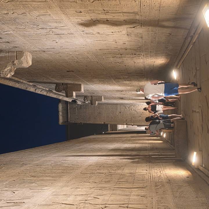 Tourists walking through narrow illuminated corridor of temple with intricate reliefs at night