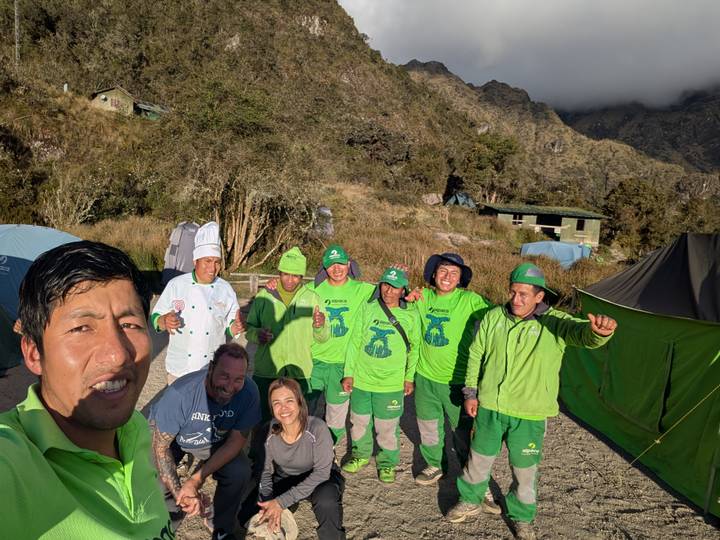 Cheerful trekking crew in bright green uniforms pose at a mountain campsite on the Inca Trail.