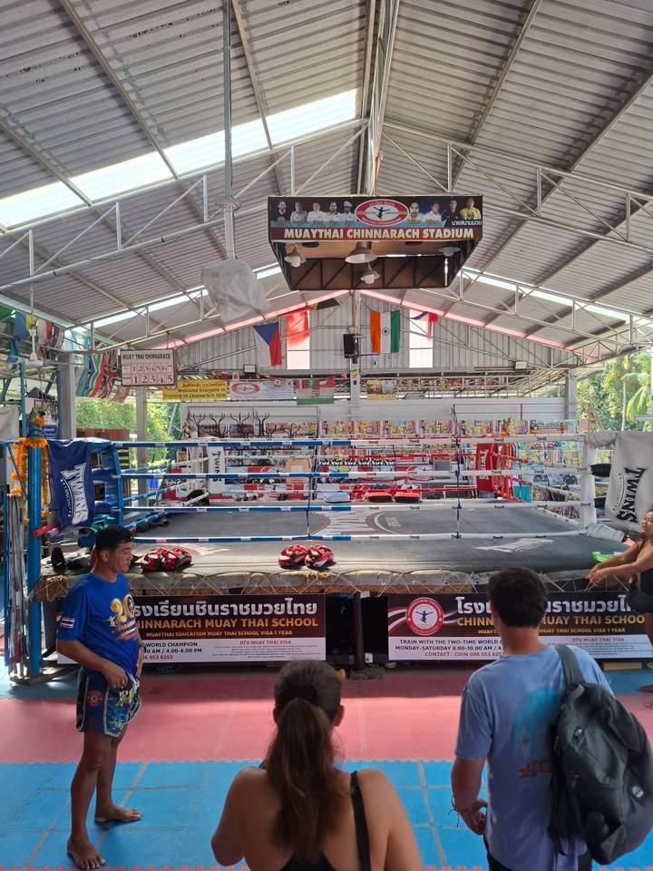 Interior of a Muay Thai boxing gym with a boxing ring, gloves and national flags hanging overhead.