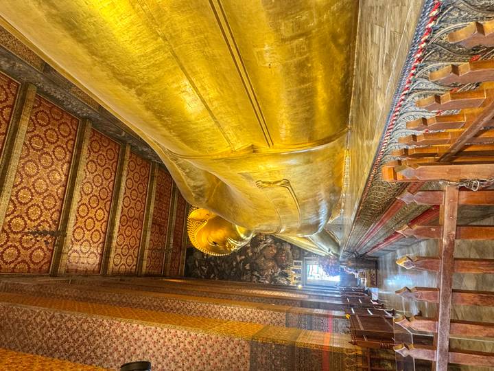 The gilded Reclining Buddha stretches along an ornate hall lined with patterned columns and mosaic ceiling panels.