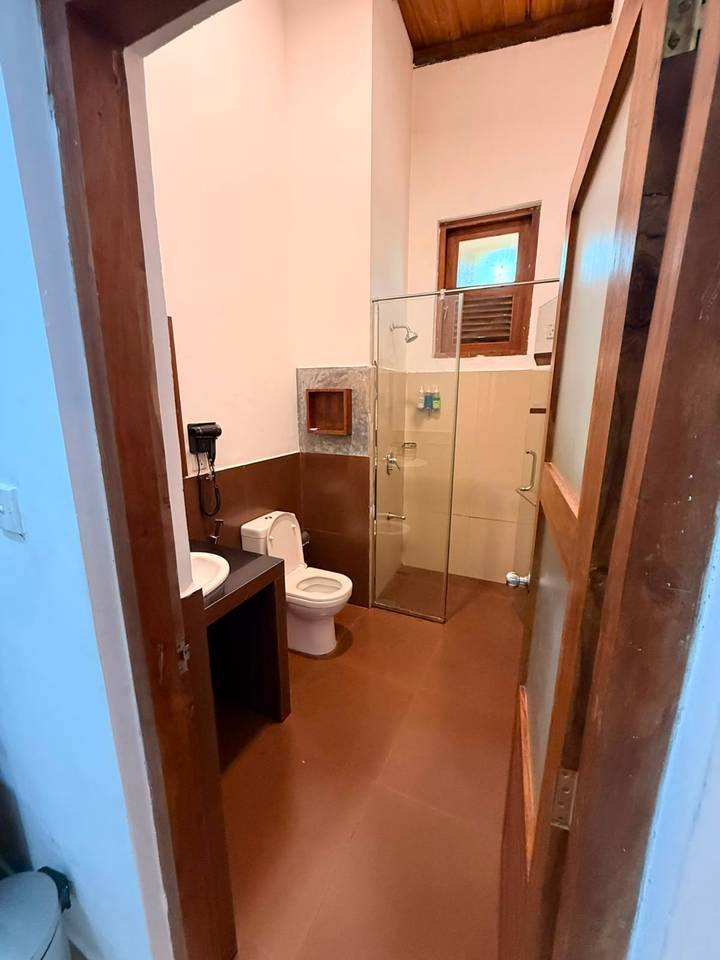 Simple hotel bathroom with glass shower enclosure, toilet and sink.