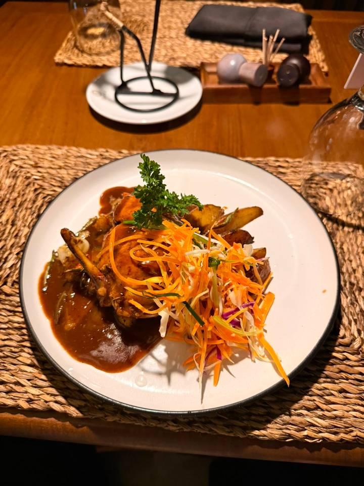 A plated main course with sauce, vegetables and garnish served on a white dish over a woven placemat.