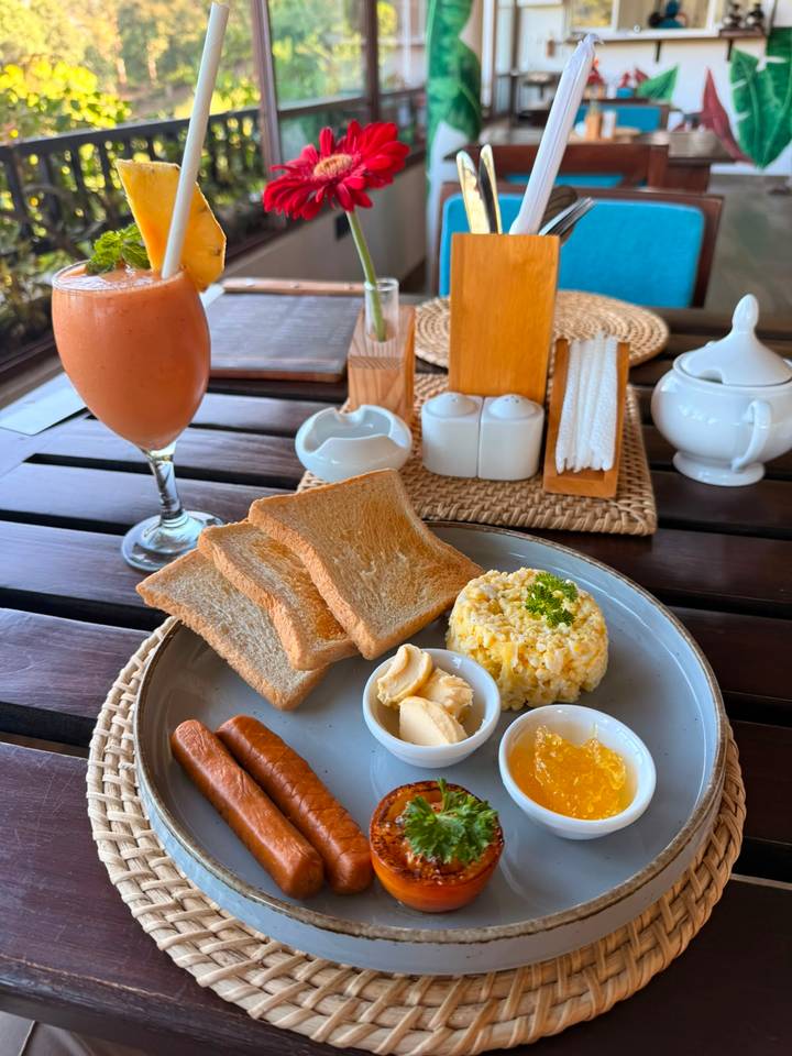 Breakfast plate with toast, scrambled eggs, butter, sausages and a fresh juice on an outdoor wooden table.