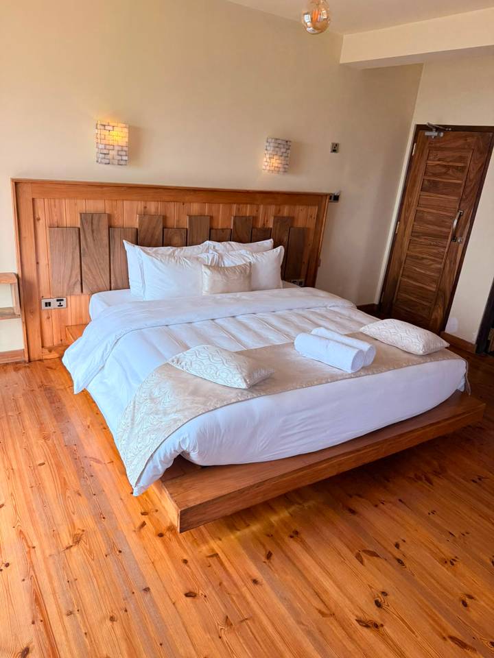 Cozy wooden-floored bedroom featuring a plush king bed with beige accents and a rolled towel.