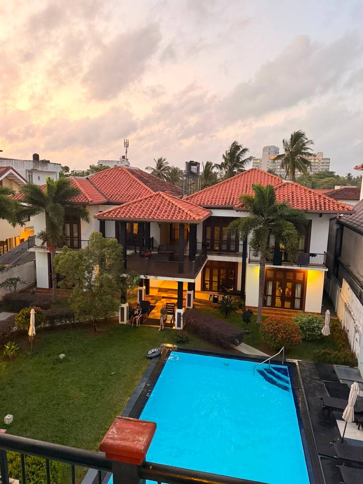 An elegant villa with red-tiled roofs, palm trees and balconies, photographed at dusk.