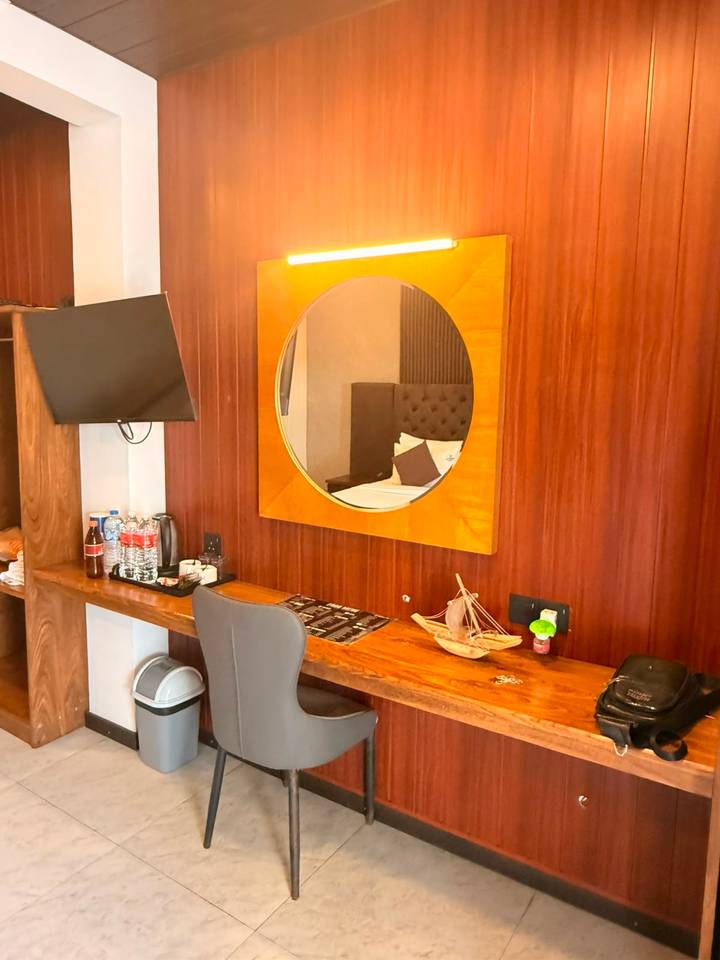 Hotel room desk area with circular mirror, TV, bottled water and decorative wooden boat model.