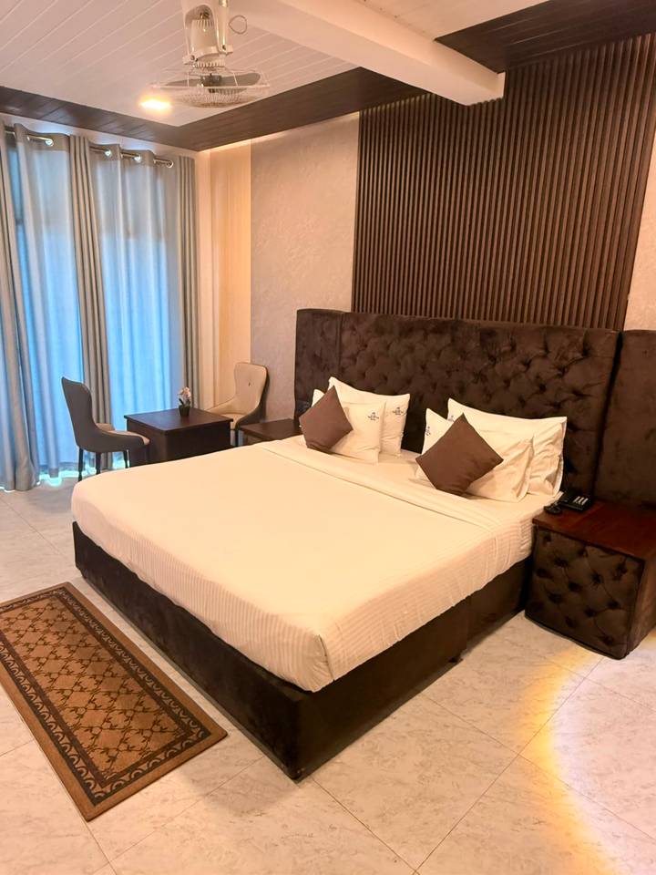 Hotel room with a large tufted headboard, crisp bedding and small table with chairs near the curtains.