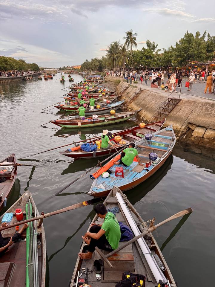 Rowers in bright green shirts prepare colorful wooden boats alongside a stone quay.
