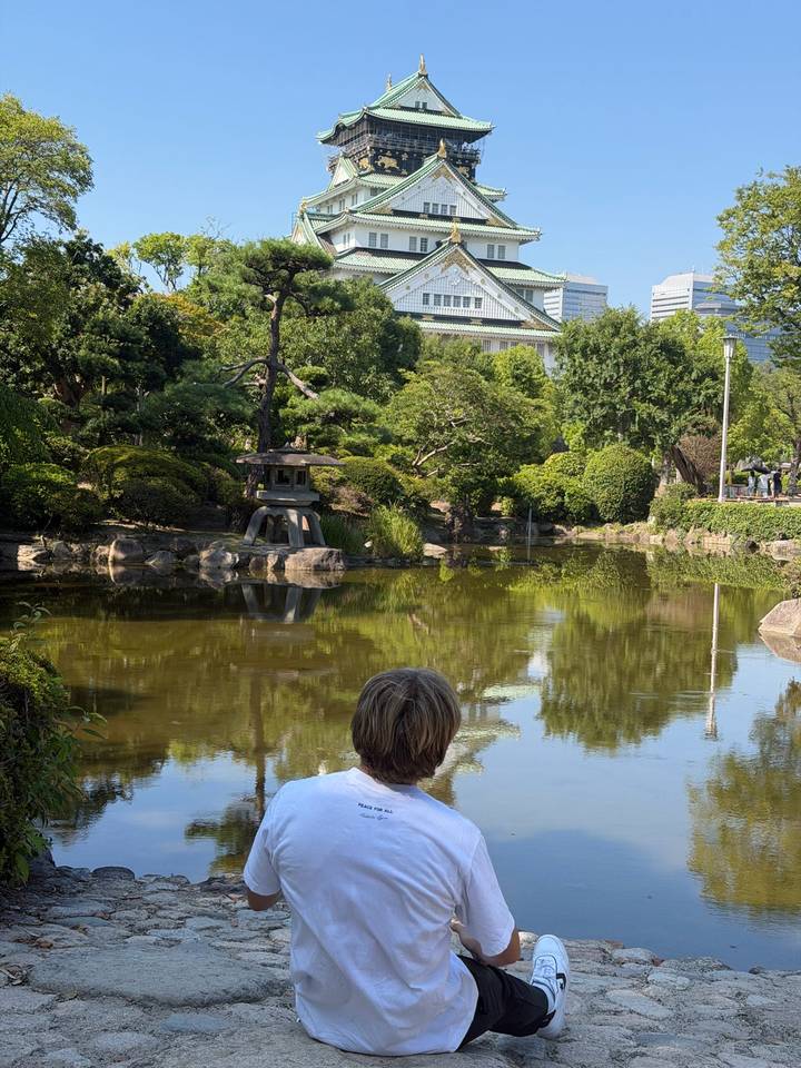 Tranquil Japanese garden pond with stone lantern and lush greenery, viewed over the head of a seated visitor.
