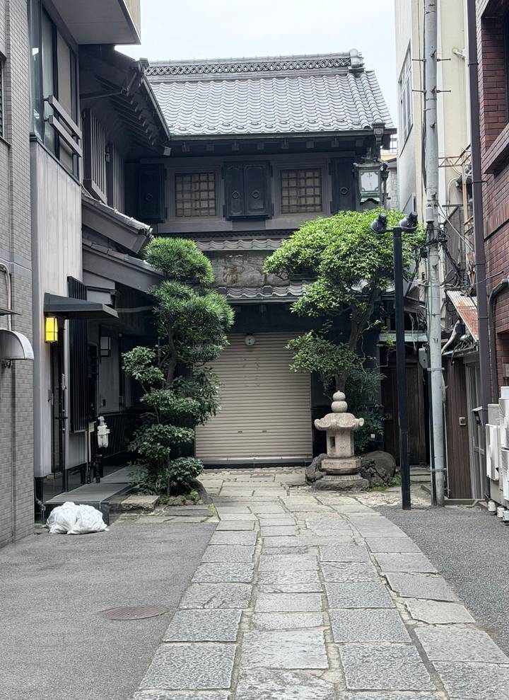 Quiet traditional Japanese alley with closed wooden shutters, manicured trees and a stone lantern.