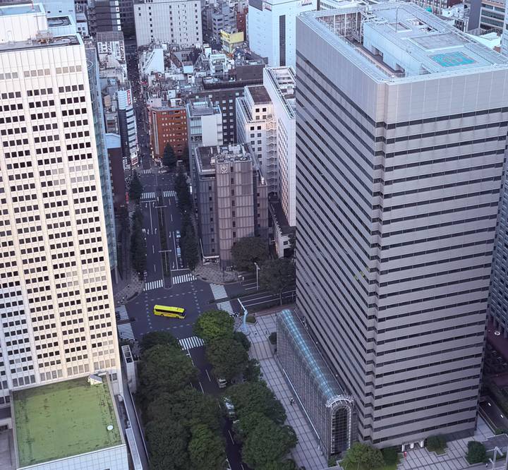 High-angle cityscape of modern skyscrapers intersected by orderly streets and a distinctive yellow bus below.