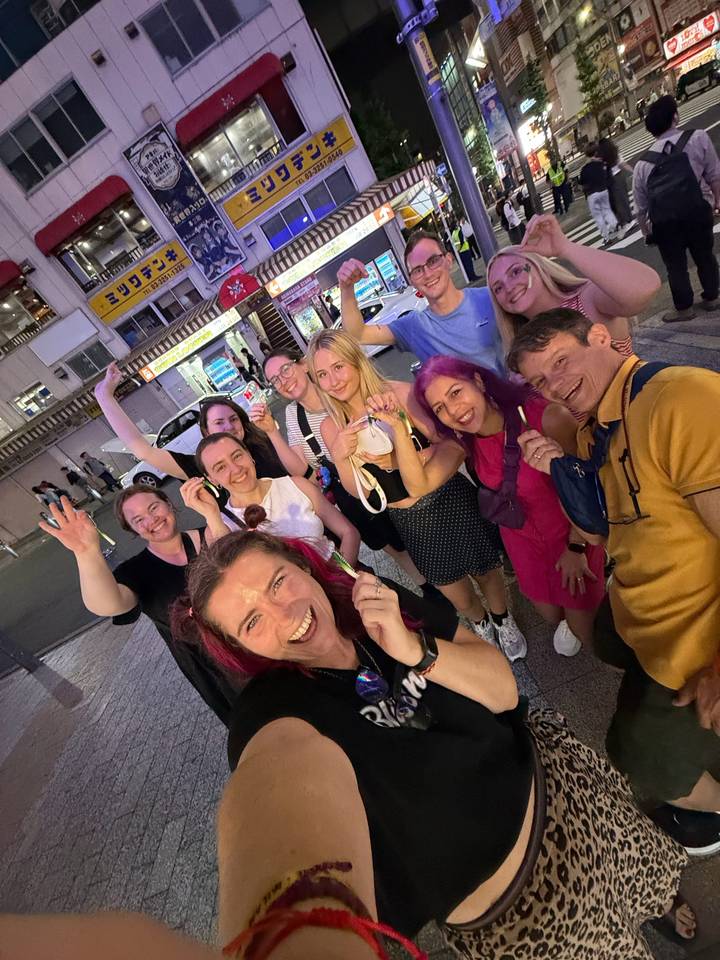 Nighttime street selfie of a cheerful travel group under neon signs in a busy Tokyo district