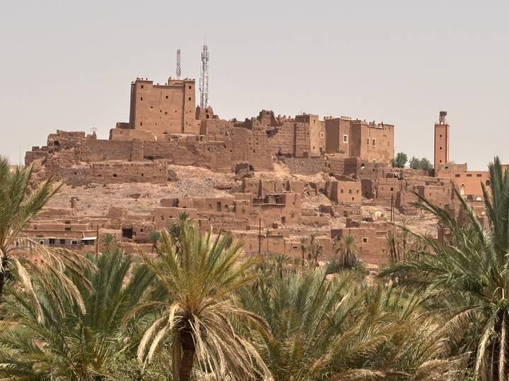 Ancient earthen kasbah fortress rising above date palms on a rocky desert hill.