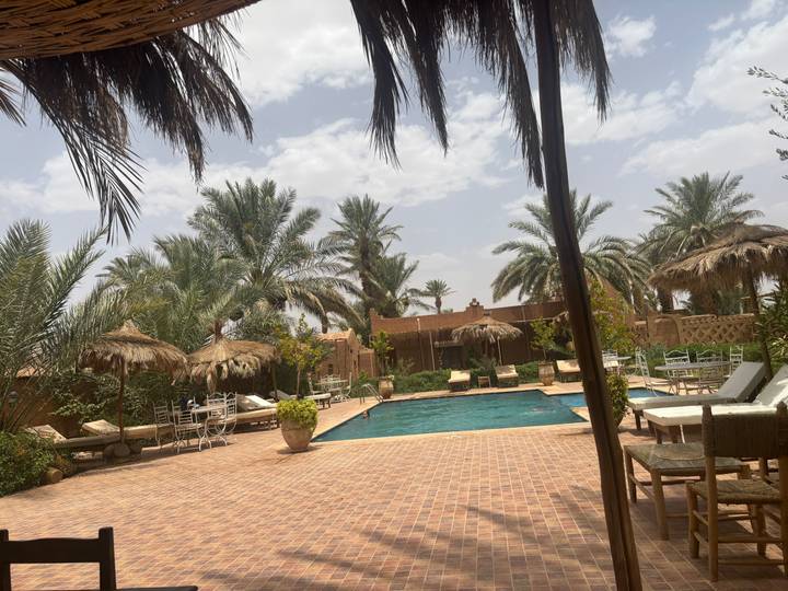 Boutique desert hotel courtyard with palm trees, straw parasols and a turquoise swimming pool.