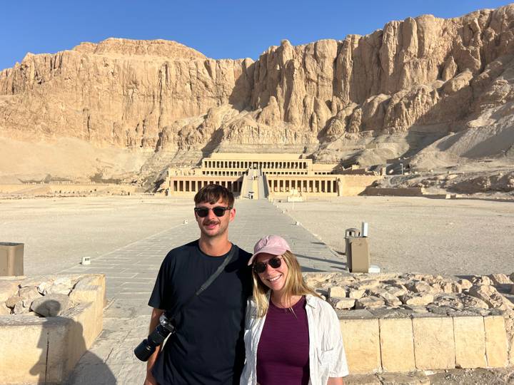 Couple standing before the grand terraces of Hatshepsut Temple carved into desert cliffs under bright sun