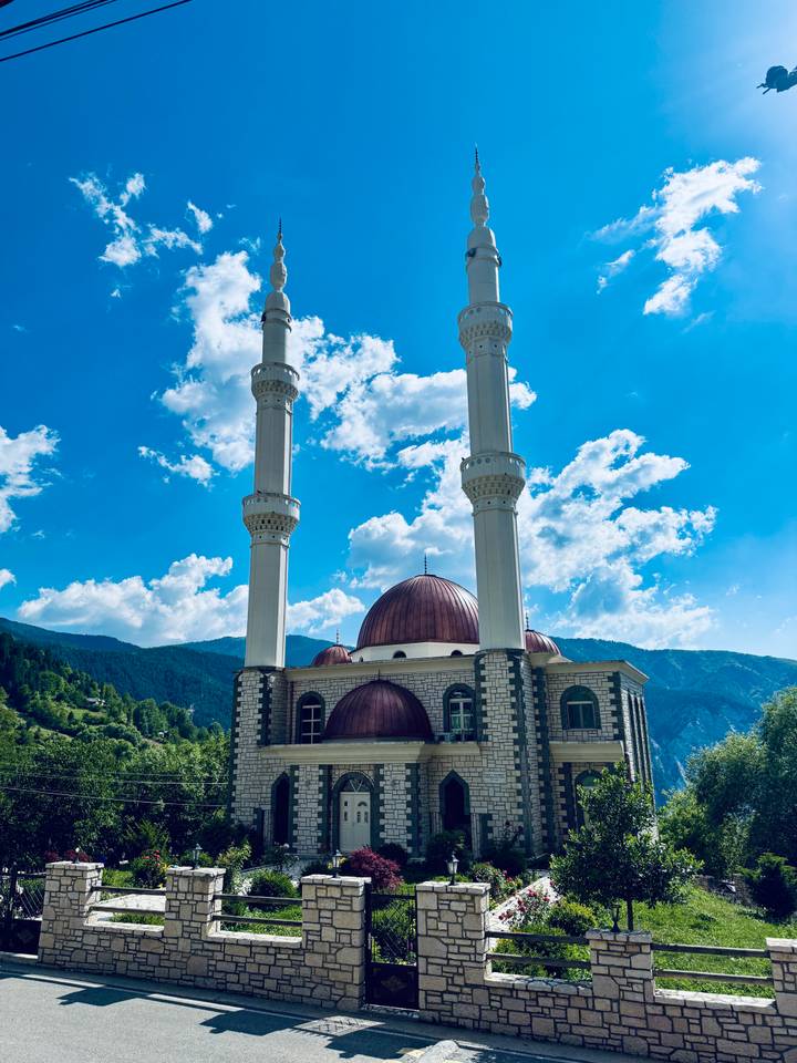 Twin-minaret mosque with rose-colored dome set against blue skies and forested mountains
