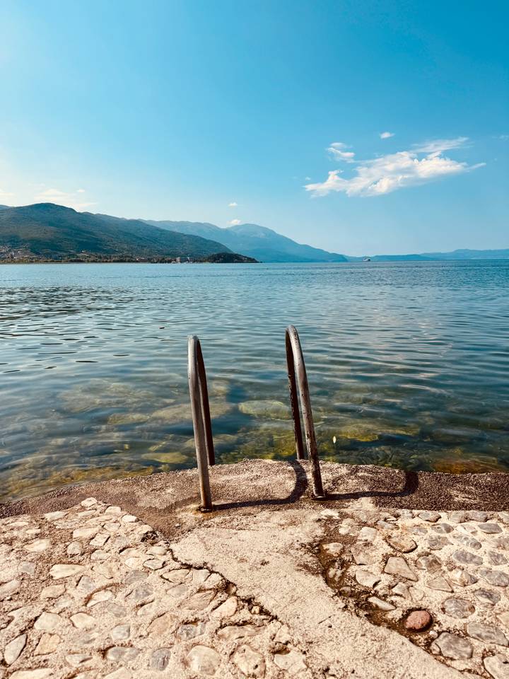 Metal ladder descending into crystal-clear lake waters with mountain shoreline in the distance