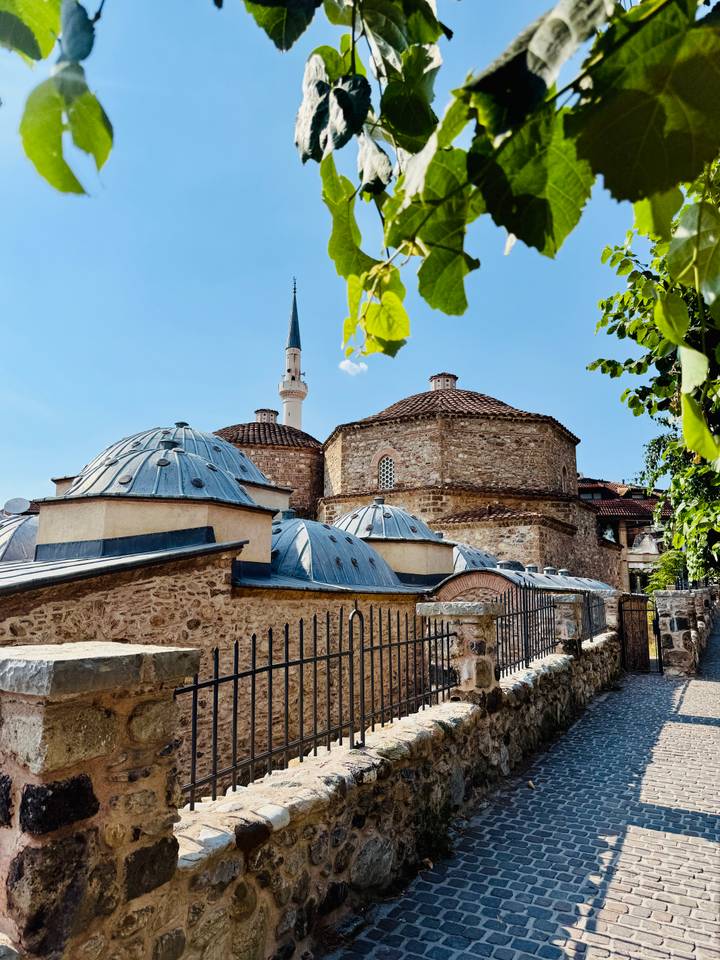 Historic stone domes and slender minaret of an Ottoman bath complex under a clear blue sky