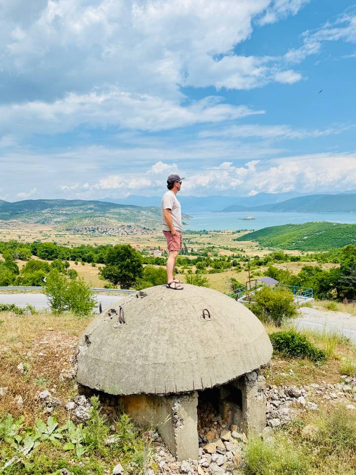 Traveler standing on a concrete bunker overlooking golden fields and a wide turquoise lake