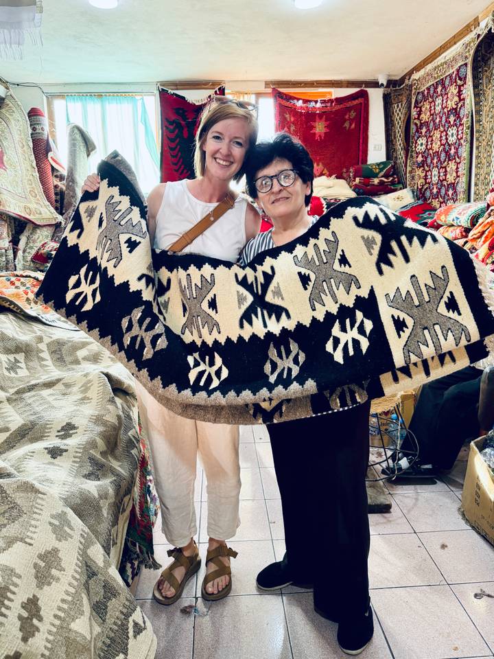 Visitor and local artisan proudly displaying a traditional black and cream woven rug in a market stall