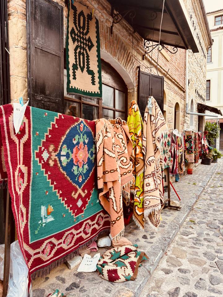 Row of brightly patterned carpets and kilims hanging outside a stone lane shop