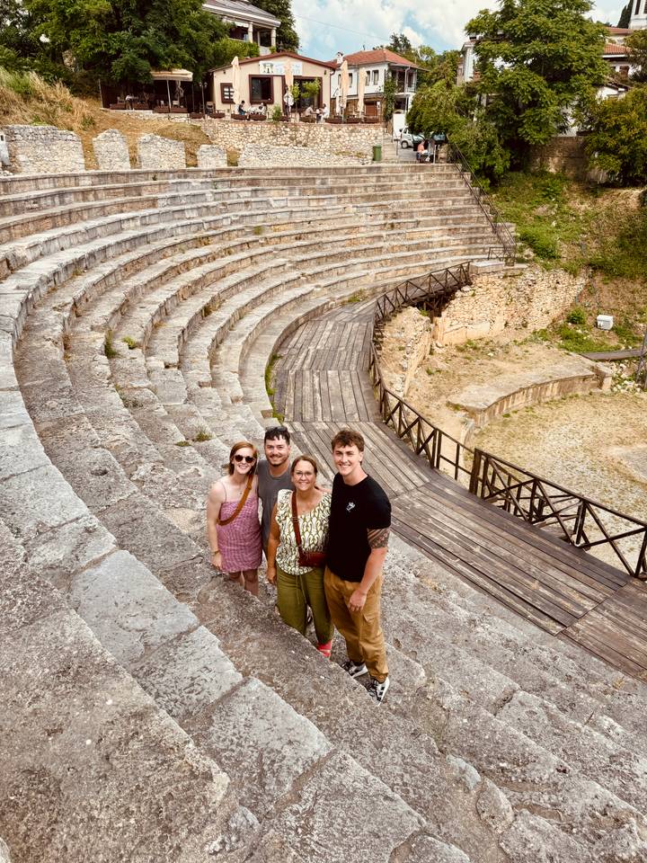 Family group smiling up from the center of an ancient stone amphitheater’s curved seating rows