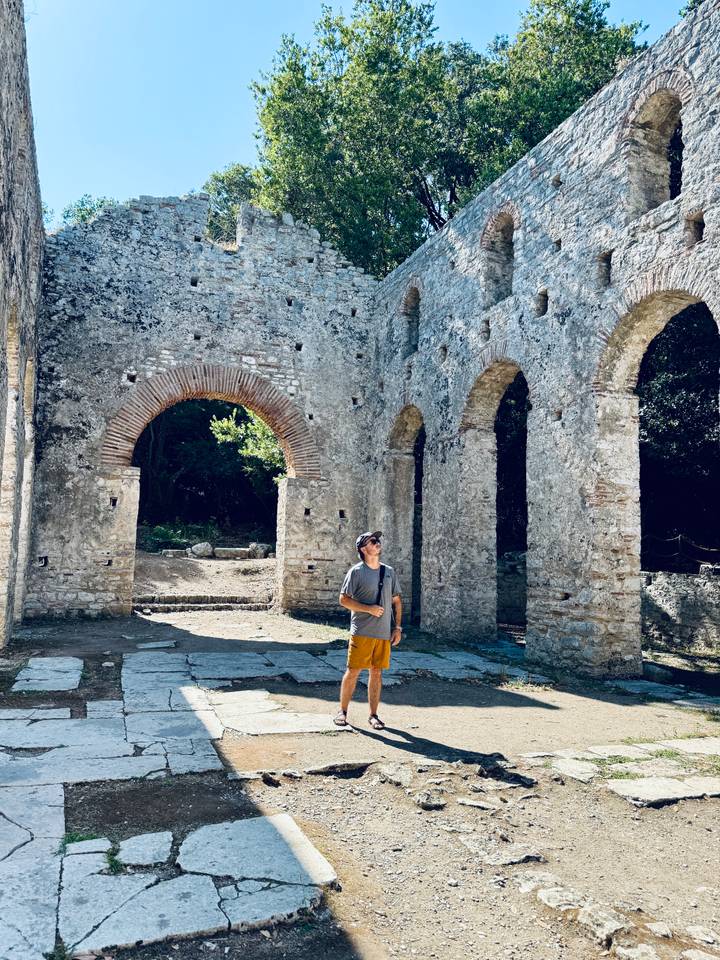 Explorer standing among towering stone arches of a historic ruined basilica surrounded by forest