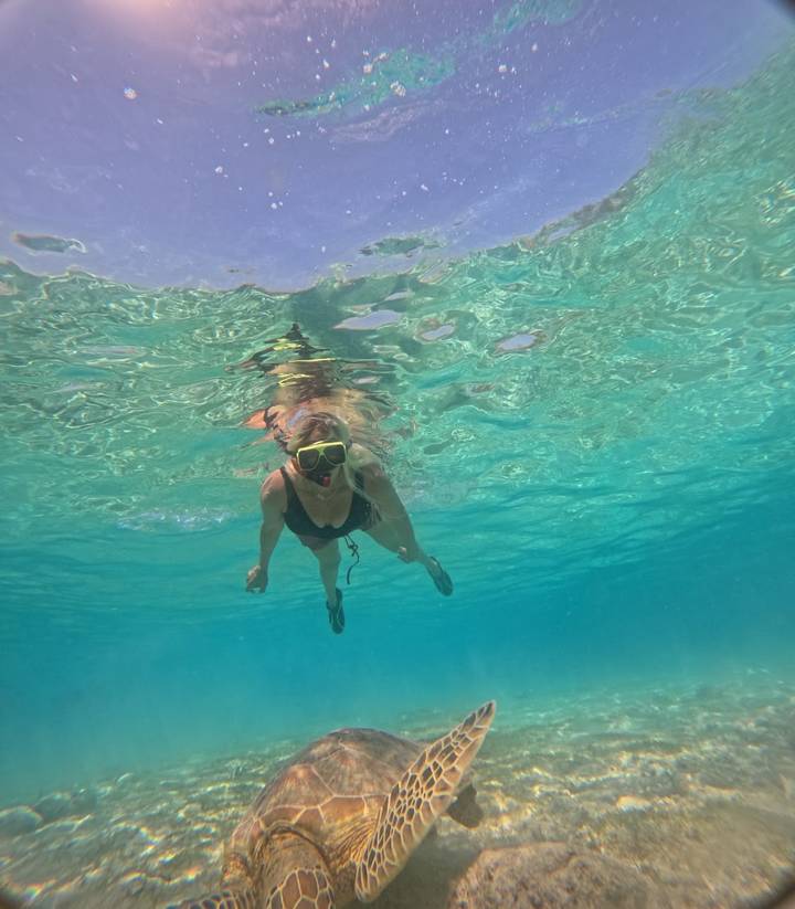 A woman snorkels underwater wearing a yellow mask in bright blue sea.