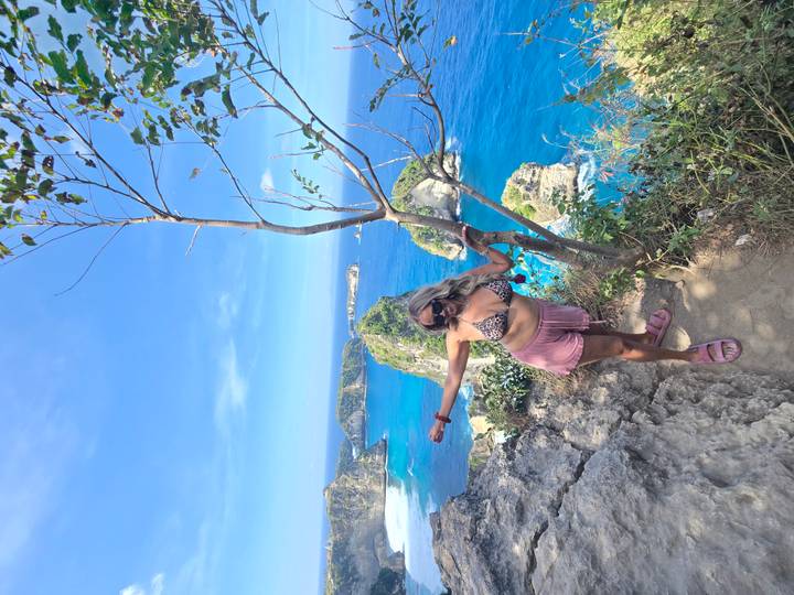 Woman stretches arms on rocky viewpoint above vivid blue sea and islands.
