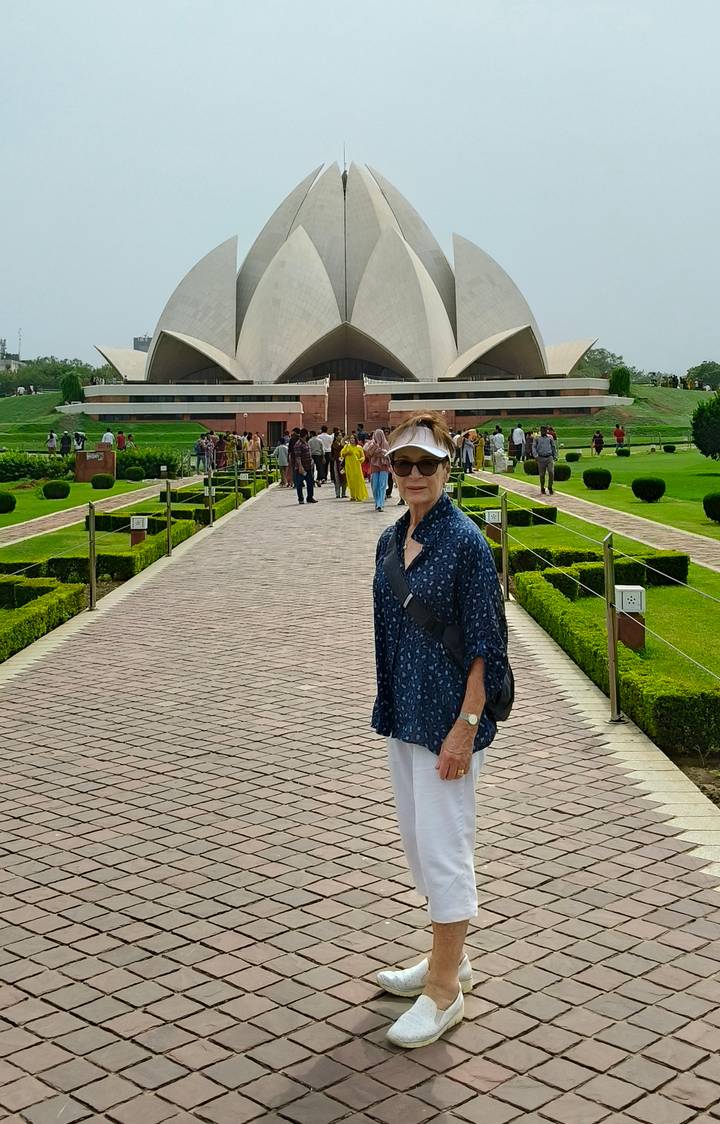 A visitor smiles on a brick walkway lined with manicured gardens leading to the Lotus Temple.