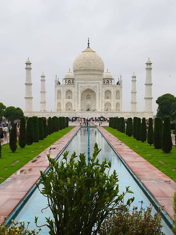 Iconic frontal view of the Taj Mahal with its reflecting pool and manicured gardens on a gray day.