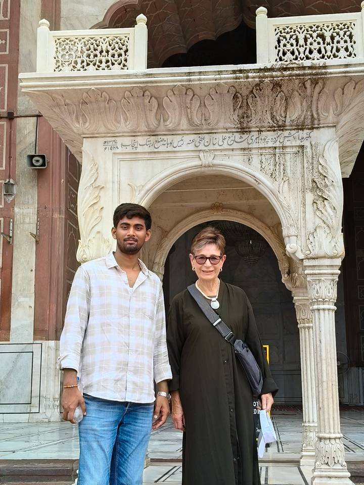 A guide and a visitor pose together beneath an ornate archway of a historic mosque.
