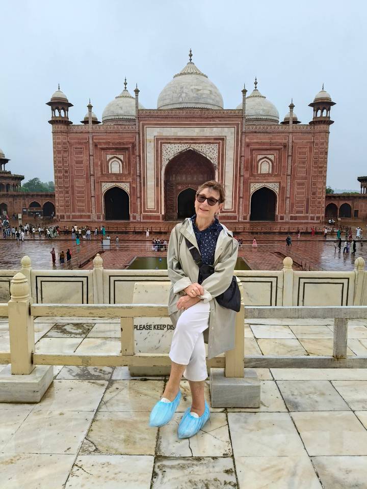 An older traveler poses on a terrace overlooking red-sandstone Mughal architecture after rain.