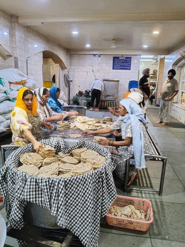 Women prepare stacks of flatbreads by hand in a bustling communal kitchen.