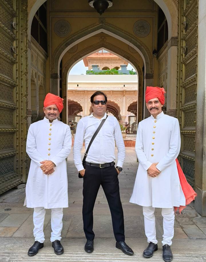 A visitor stands between two traditionally dressed doormen in white uniforms and red turbans.