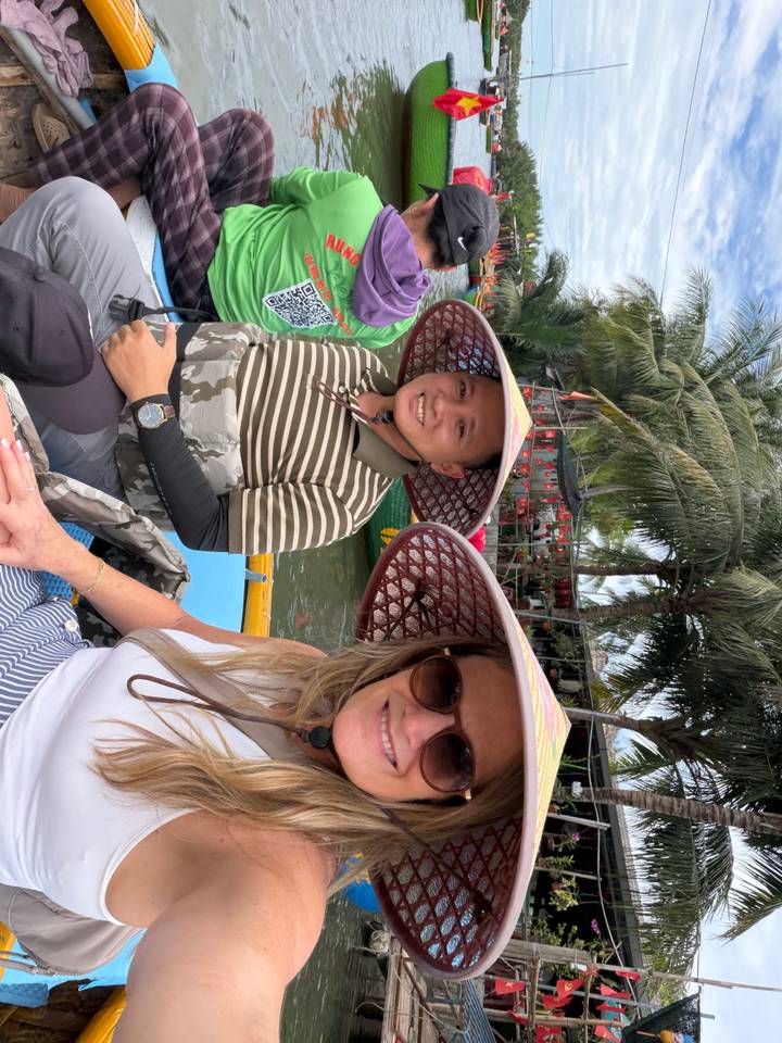 Smiling guide and tourist wearing broad-brim hats in a small river boat under palms.