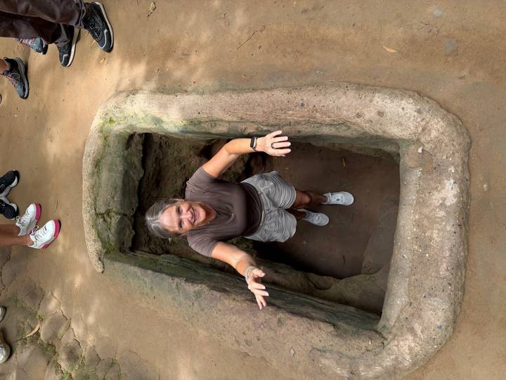 Visitor emerging from a narrow Cu Chi tunnel entrance carved into the ground.