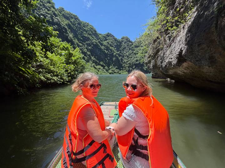 Two women in orange life jackets aboard a small raft between towering limestone cliffs.