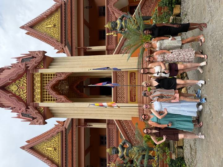 Women’s group stands in front of an ornate Khmer temple façade holding national flags.