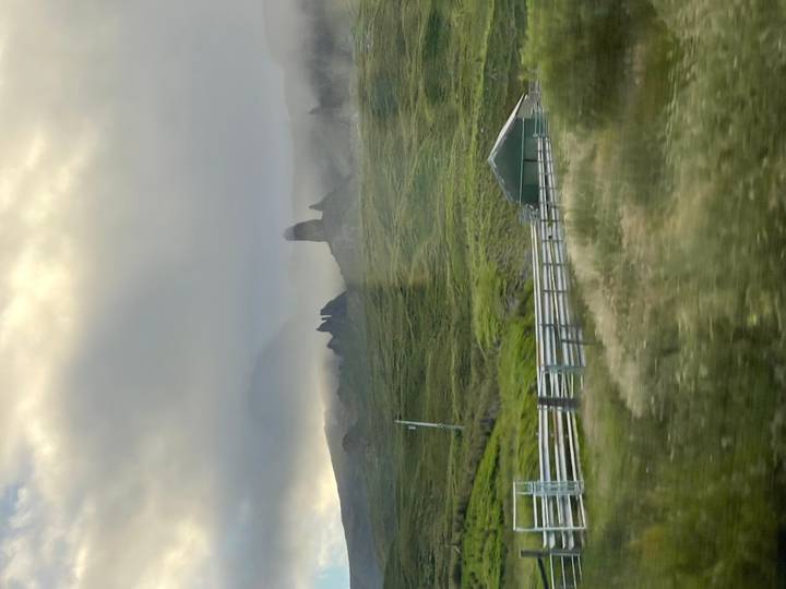 Misty outline of the Old Man of Storr rock pinnacles rising above green slopes under low clouds.