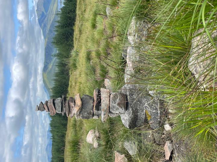 Stacked stone cairn stands on grassy moorland with blue-green mountains in the distance.