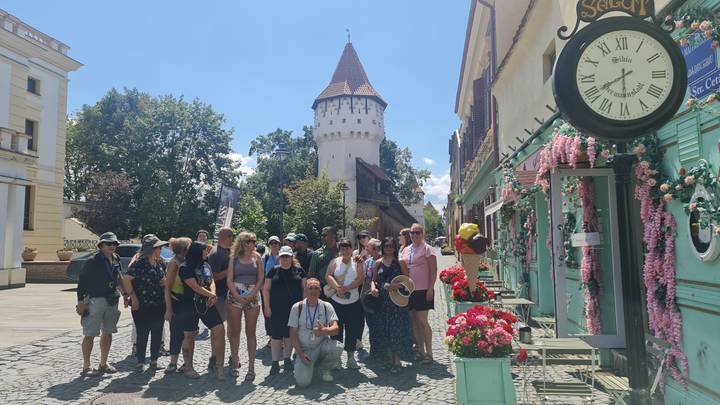 Tour group posing on a cobblestone street lined with pastel buildings and a medieval tower in the background.