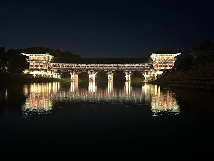 Illuminated Woljeong Bridge reflecting perfectly on calm water at night.