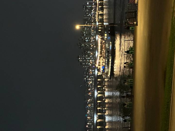 Night view of a lit cruise boat on the Han River with apartment towers and bridge lights in the background.