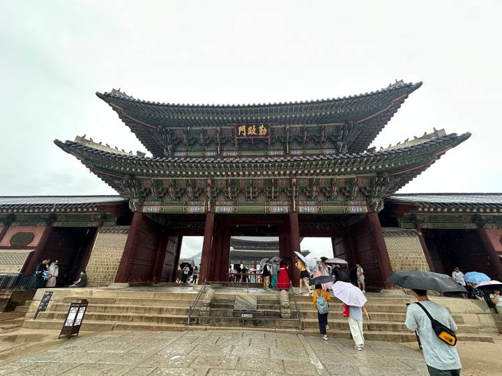 Visitors with umbrellas entering the main gate of Gyeongbokgung Palace on a rainy day.