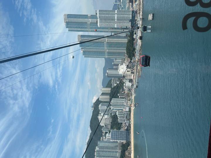Cable cars gliding above blue sea towards a modern skyline of Busan under bright skies.
